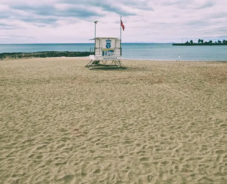Izada la bandera roja en la Playa de El Reducto, Al fondo a la derecha la Punta del Camello donde el Consorcio del Agua y Canal Gestión tienen en aliviadero del emisario, originario de la contaminación