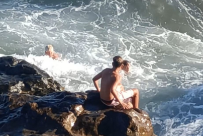 Personas bañándose en una playa de piedras.