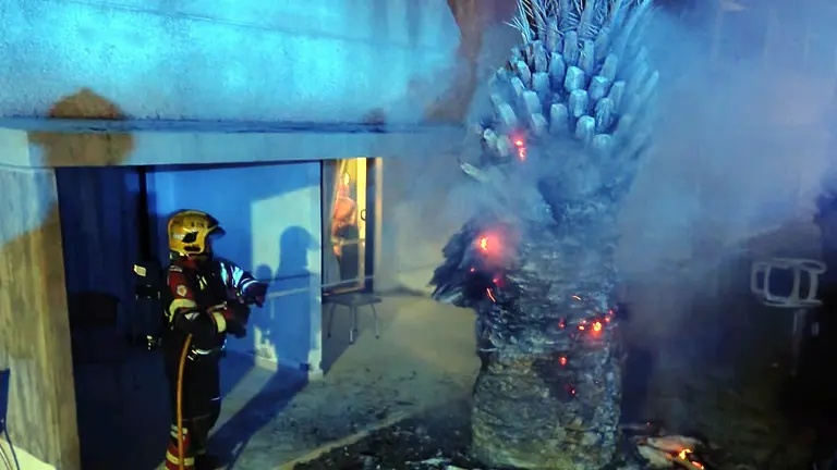 Los bomberos apagan el fuego mientras un turista se asoma desde su habitación