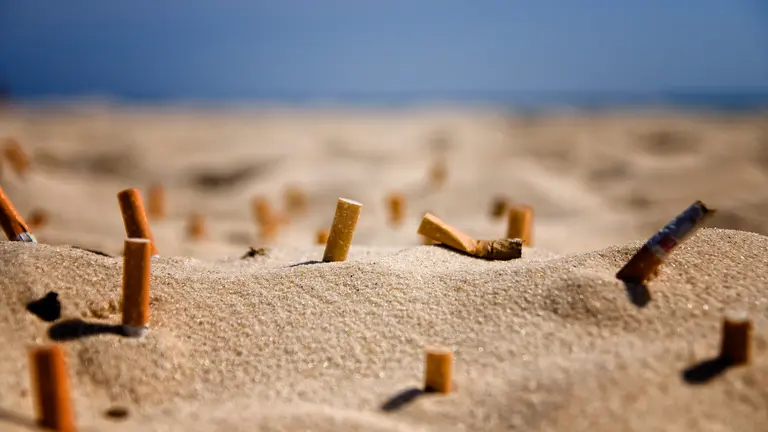 Colillas de cigarrillos en la arena de una playa.